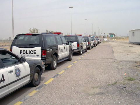 1999 Mercury Grand Marquis - Several Kuwait police vehicles are parked in a line on the side of a road.