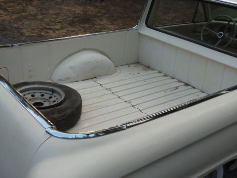 1963 Ford Ranchero - The interior of a white pickup truck bed shows a spare tire and ribbed flooring.