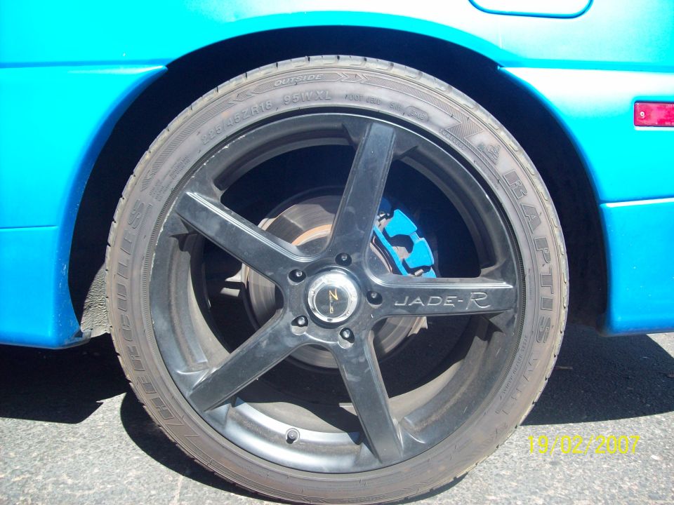Blue car's black five-spoke wheel with a bright blue brake caliper visible behind it