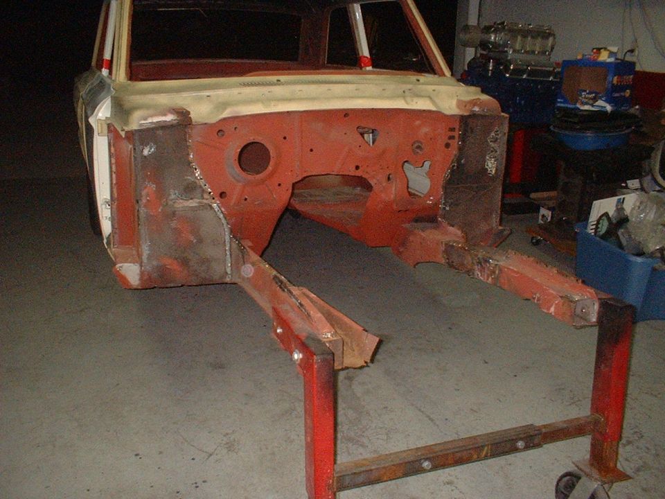 1964 Ford Fairlane body shell on a stand, showing exposed engine bay and frame rails, in a workshop