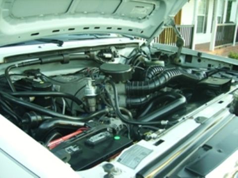 1995 Ford Bronco - The engine compartment of a white vehicle is shown with the hood open, revealing various engine components and wiring.