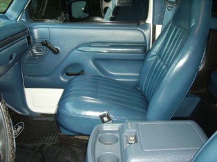 1995 Ford Bronco - Interior view of a truck's blue seats and door panel, showing the center console and floor mat.