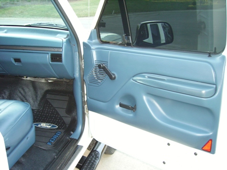 1995 Ford Bronco - Close-up of the blue interior of a vehicle, showing the door panel, dashboard, and a Ford-branded floor mat.