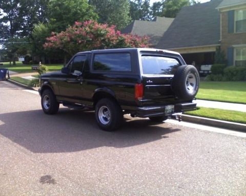 1996 Ford Bronco - A black Ford Bronco is parked on a residential street with a house and trees in the background.