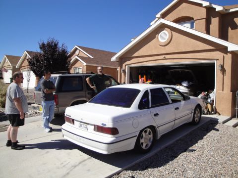 1989 Ford Taurus - A white 1989 Ford Taurus is parked in a driveway, with two men standing nearby and another vehicle in the garage.