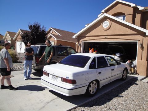 1989 Ford Taurus - A white 1989 Ford Taurus sedan is parked in a driveway next to an SUV and a garage.