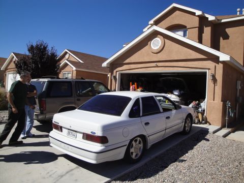 1989 Ford Taurus - White 1989 Ford Taurus parked in front of a garage with an SUV behind it.