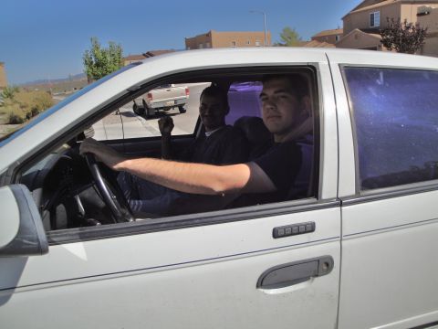 1989 Ford Taurus - Two men are inside a white sedan, with a pickup truck in the background.