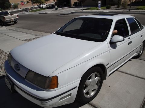 1989 Ford Taurus - A white sedan is parked on a driveway. The vehicle is viewed from the front quarter angle.