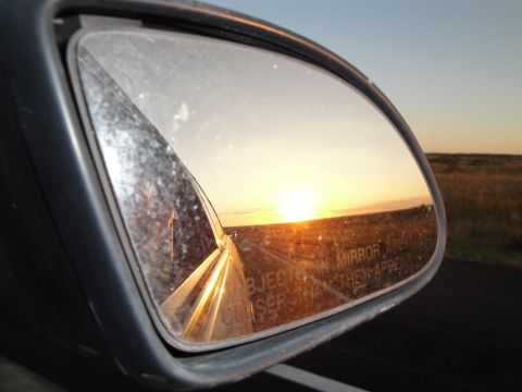 1989 Ford Taurus - Sunset viewed in a car's side mirror, reflecting the open road and a vast, golden landscape.