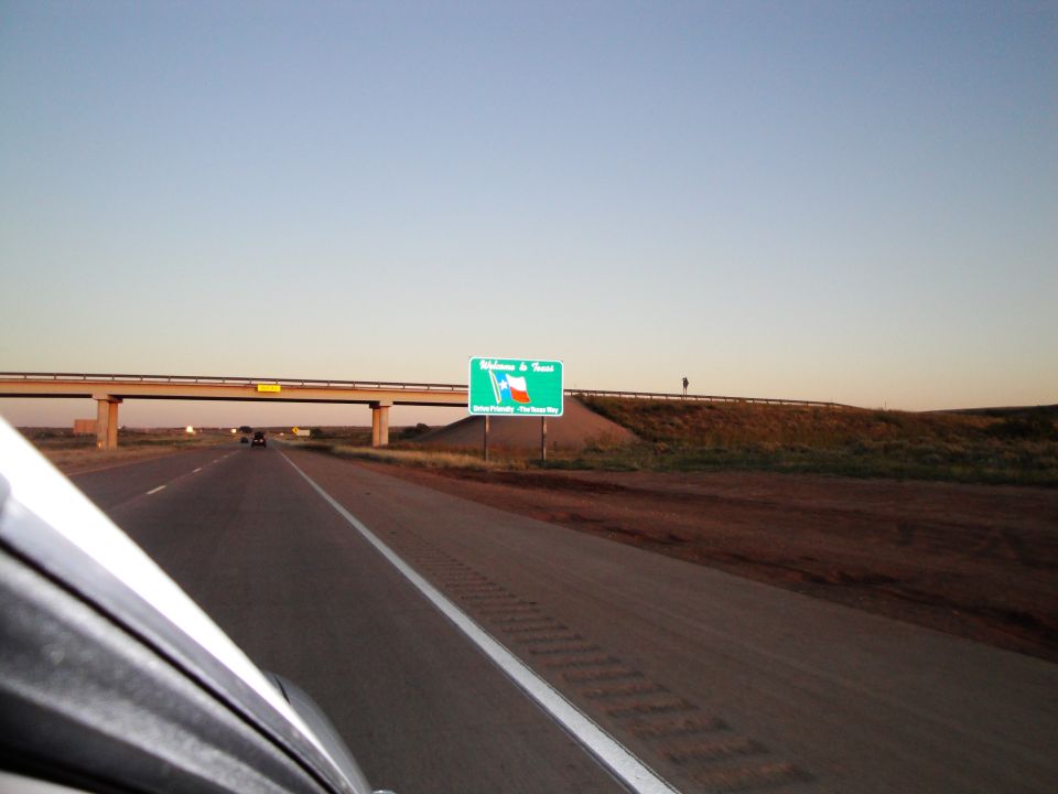 Highway scene with a green welcome to Texas sign and a bridge overhead