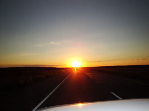 1989 Ford Taurus - A scenic view of a highway disappearing into the horizon as the sun sets, captured from the perspective of a moving vehicle.