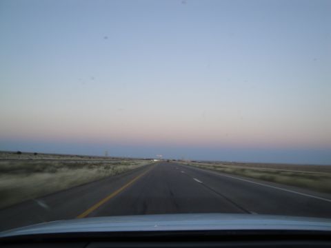 1989 Ford Taurus - The view from the driver's seat shows a long, straight highway stretching towards the horizon under a fading sky.
