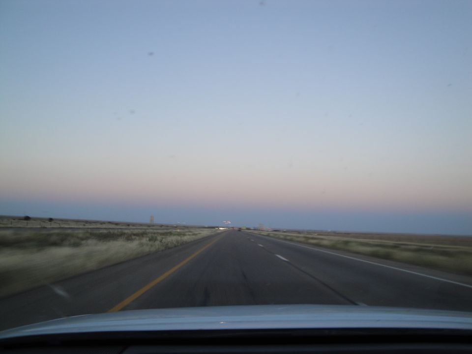 Driving on a highway with a wide, clear sky at dusk. Dry grass lines the sides of the road