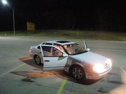 1989 Ford Taurus - A white 1989 Ford Taurus sedan is parked at night with its doors and sunroof open.