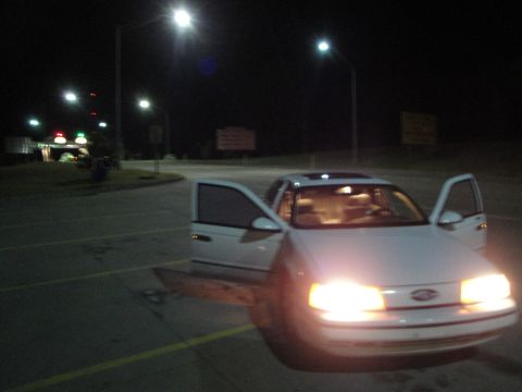 1989 Ford Taurus - A white 1989 Ford Taurus is parked with its doors open at night, illuminated by streetlights.