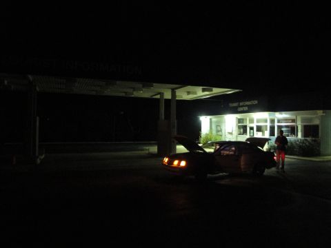 1989 Ford Taurus - A person stands near a car with its hood and trunk open at a tourist information center after dark.