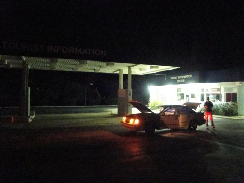 1989 Ford Taurus - A car with its hood and trunk open sits under a covered area at a tourist information center at night.