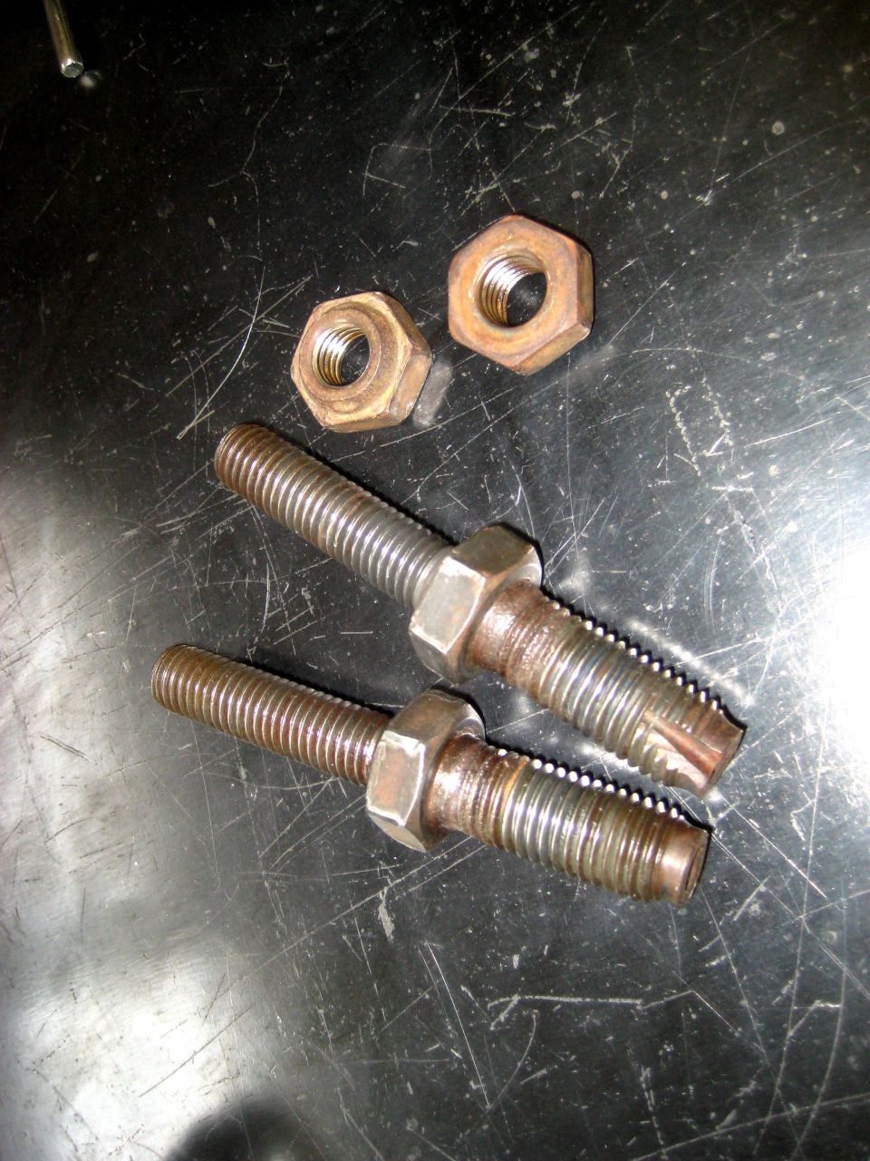 Two threaded bolts with hex nuts on them, resting on a scratched surface