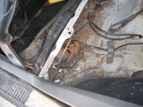 1992 Jeep Cherokee - The interior floor of a vehicle exhibits significant rust and exposed wiring, indicating poor condition.
