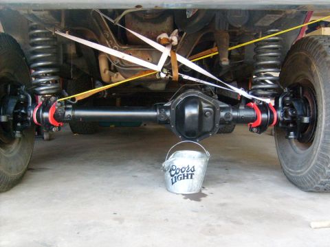 1986 Ford Bronco - A close-up view of a vehicle's undercarriage, focusing on the differential and suspension system, with a Coors Light bucket placed nearby.