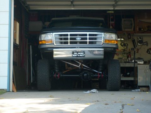 1986 Ford Bronco - Front view of a black lifted Ford truck with a chrome grille and bumper, parked inside a garage.
