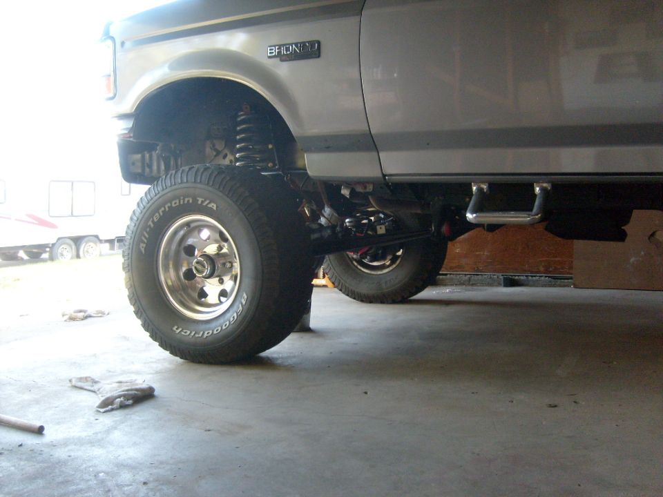 Side view of a silver Ford Bronco with aftermarket wheels and tires. The "BRONCO" badge is visible
