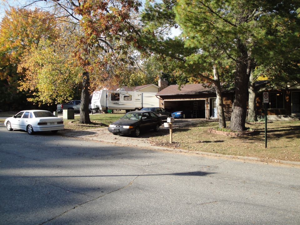 White sedan parked on street, side view, with a dark sedan and RV in the background