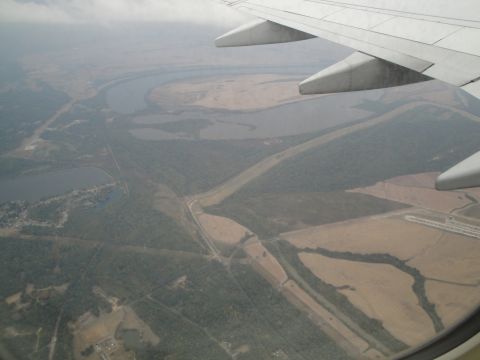 1989 Ford Taurus - An aerial perspective captures a meandering river and surrounding terrain, partially obscured by clouds and an airplane's wing.