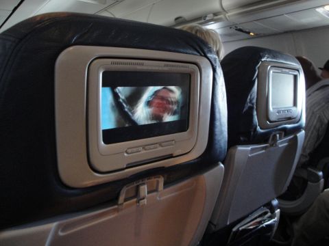 1989 Ford Taurus - View of an airplane cabin showing seatback entertainment screens, with one screen displaying a partial image of a person.
