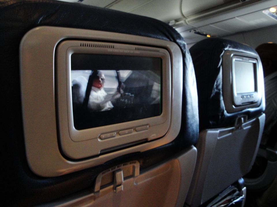 Airplane interior with two seatback screens displaying movies