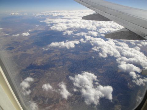 1989 Ford Taurus - Looking down at the earth from an airplane, with clouds scattered across the landscape.