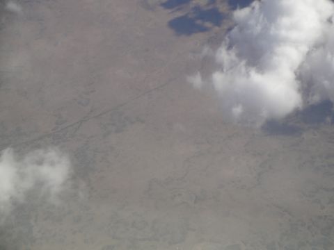 1989 Ford Taurus - An aerial perspective captures a vast, dry terrain marked by a meandering riverbed and sparse greenery, partially obscured by clouds.