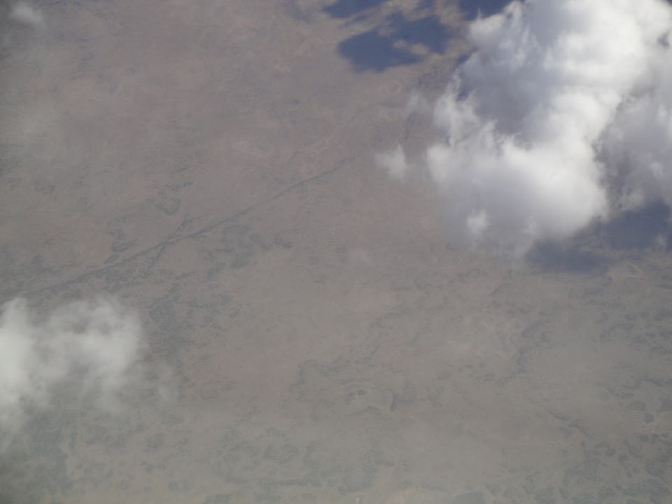 Aerial view of a dry, arid landscape with scattered vegetation and a winding riverbed under a cloudy sky