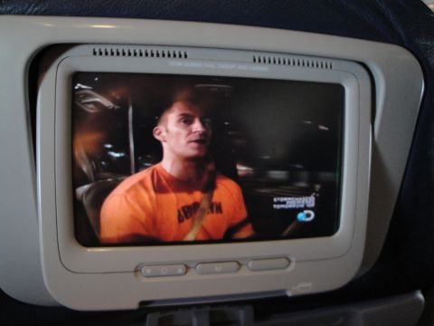 1989 Ford Taurus - A man wearing an orange shirt drives a car at night, with a television screen showing the scene.