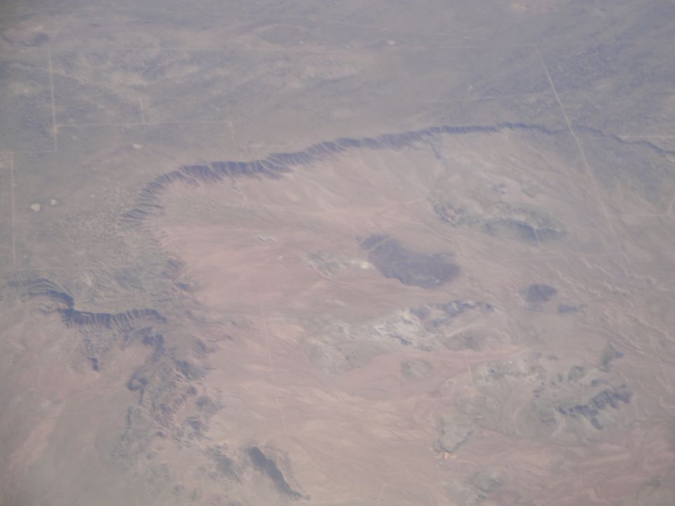 Aerial view of a vast desert landscape with eroded mesas and canyons under a hazy sky
