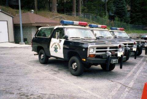 1987 Dodge 1500 - Row of Dodge Ramcharger police vehicles, likely from the 1980s, parked outside a building.