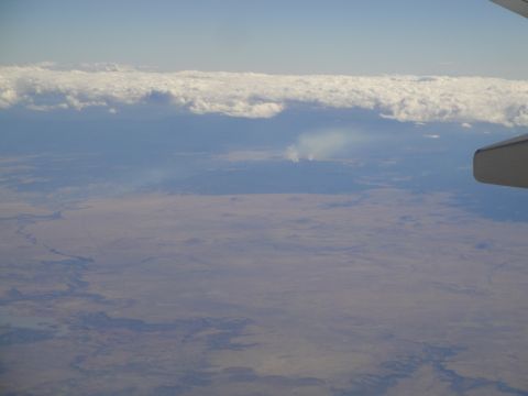 1989 Ford Taurus - An aerial perspective captures distant smoke plumes rising from the earth beneath a layer of clouds, as seen from an aircraft.