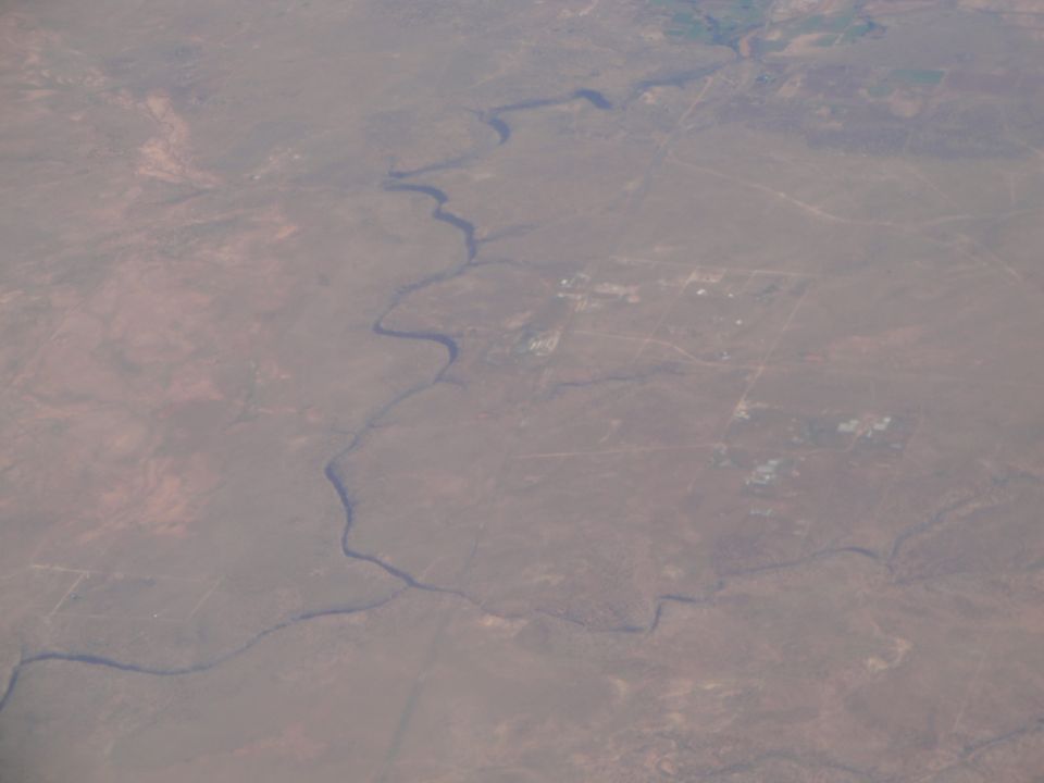Aerial view of a winding river through a dry, sparsely populated landscape with scattered buildings