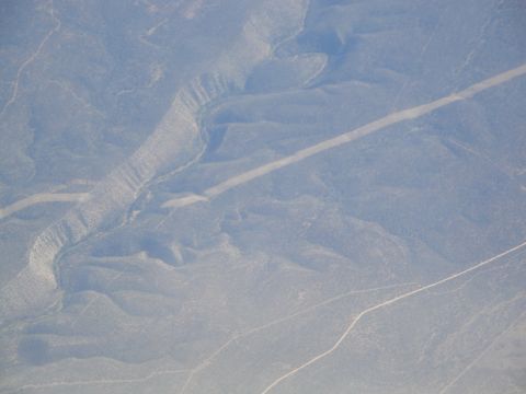 1989 Ford Taurus - A road snakes through a desolate, arid terrain under a hazy sky.