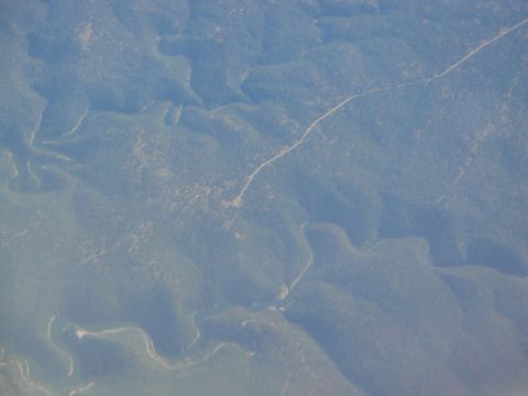 1989 Ford Taurus - An aerial perspective captures the undulating terrain of forested hills, bisected by a solitary, winding road.