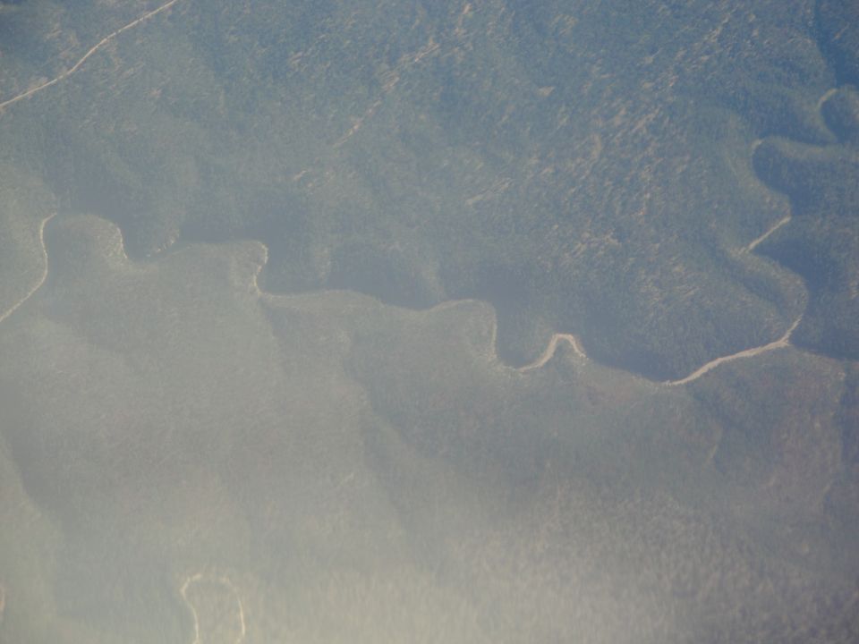 Aerial view of a river snaking through dense, green hills under a hazy sky