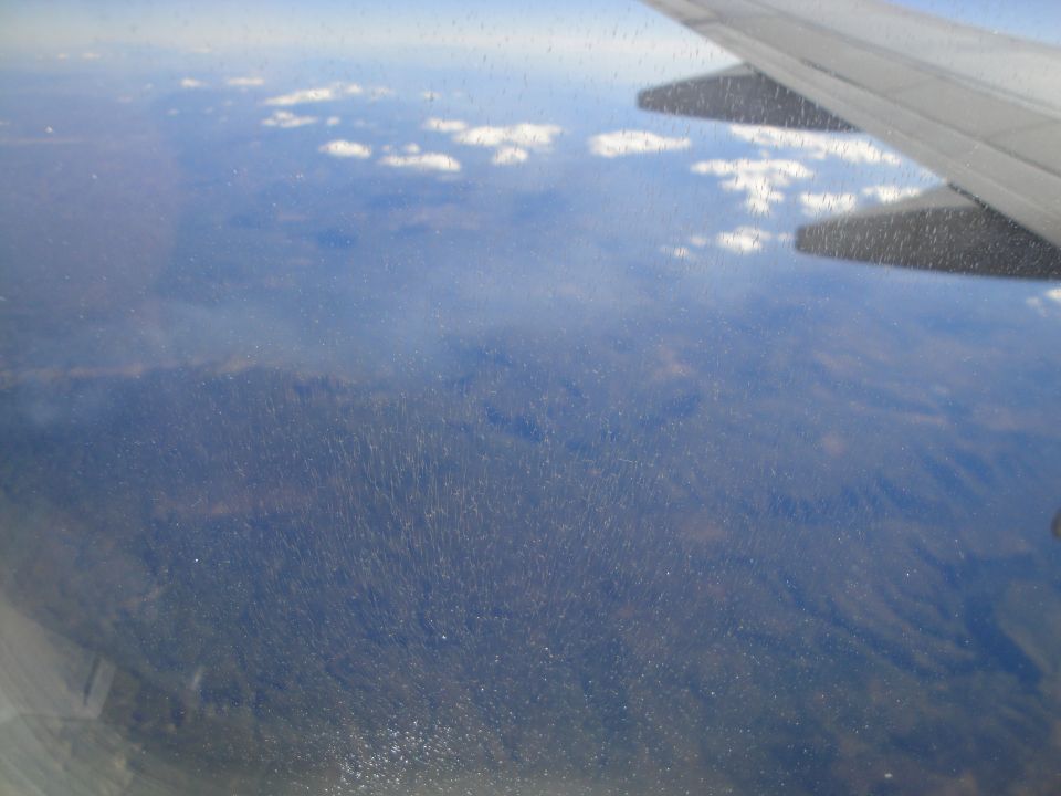 Airplane wing seen from window above forested landscape with clouds