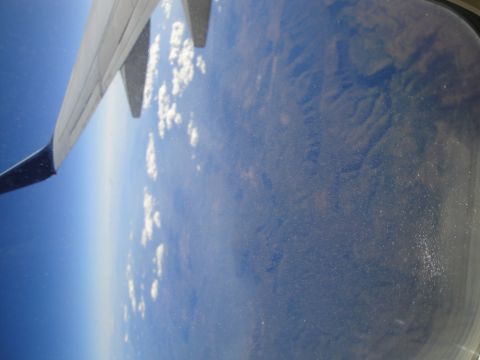 1989 Ford Taurus - View from an airplane window showing the wing, clouds, and terrain below.