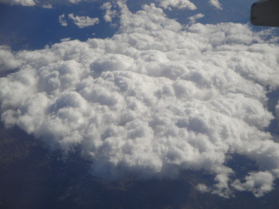 View of cumulus clouds from an airplane window, with land visible below