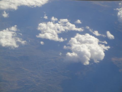 1989 Ford Taurus - An aerial view shows scattered clouds drifting over a vast, arid terrain under a clear blue sky.
