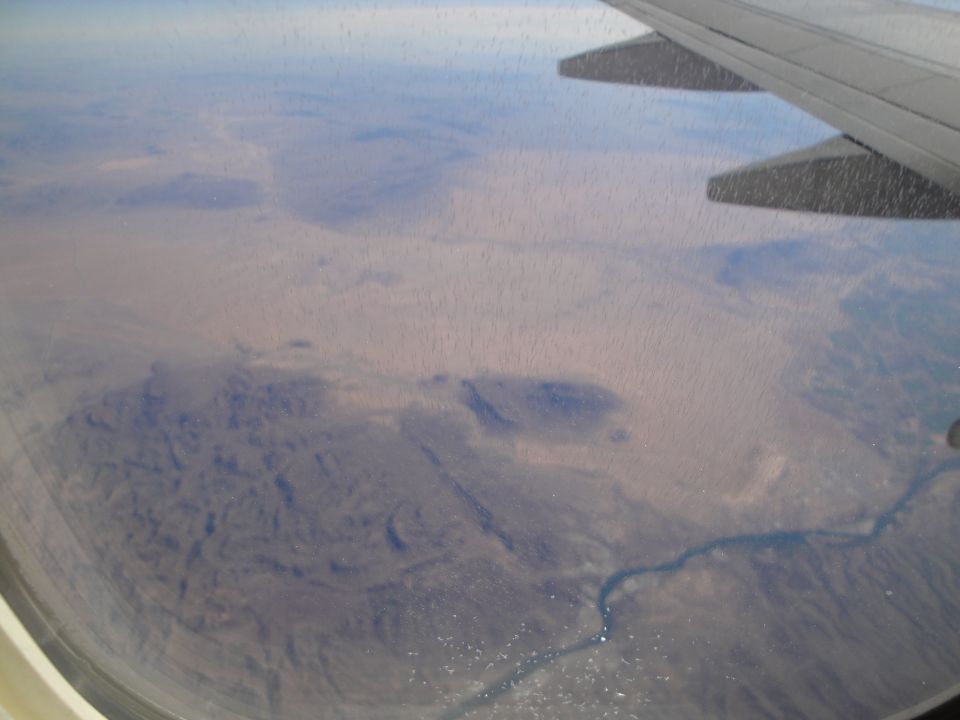 Airplane wing above desert landscape with a river and scattered buildings