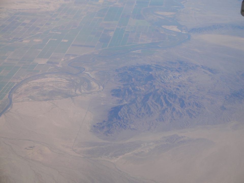 Aerial view shows a winding river next to rectangular agricultural fields and mountains