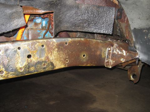 1979 Ford Bronco - Close-up view of a heavily rusted vehicle frame rail, showing the engine block and part of the suspension system.