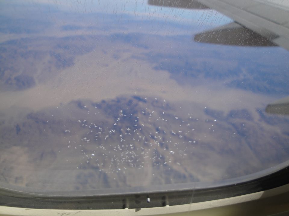 Aerial view through an airplane window of a dusty desert landscape with scattered white objects
